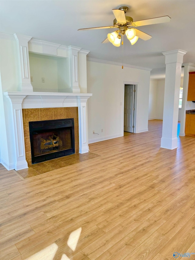 unfurnished living room with light wood finished floors, ornamental molding, a tile fireplace, and decorative columns