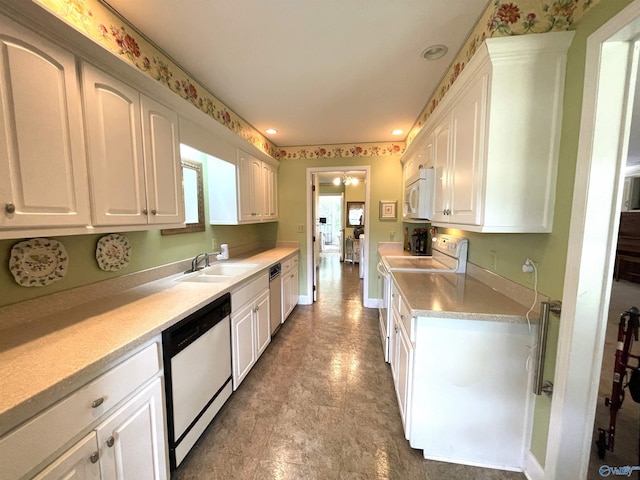 kitchen featuring white appliances, baseboards, light countertops, white cabinetry, and a sink