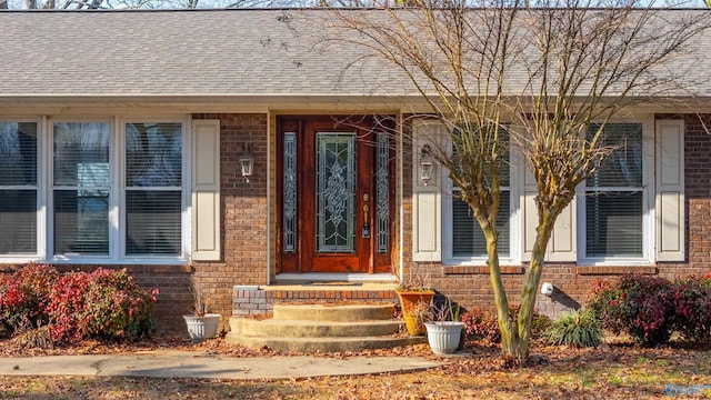 doorway to property with brick siding and roof with shingles
