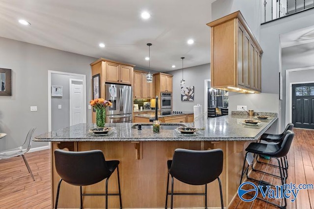 kitchen with sink, hanging light fixtures, light hardwood / wood-style flooring, kitchen peninsula, and stainless steel fridge