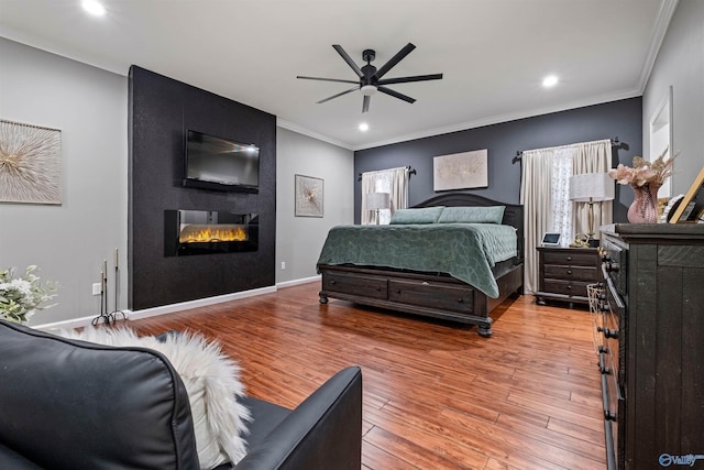 bedroom featuring a large fireplace, light hardwood / wood-style floors, ceiling fan, and crown molding