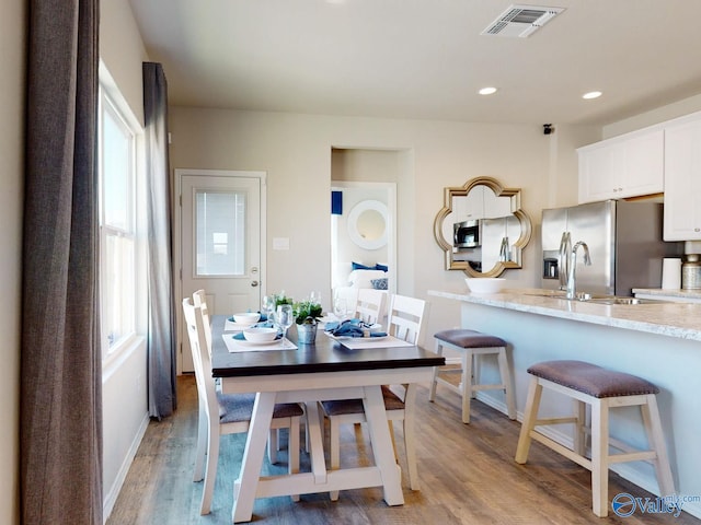 kitchen with white cabinetry, a kitchen bar, stainless steel fridge with ice dispenser, a healthy amount of sunlight, and light wood-type flooring