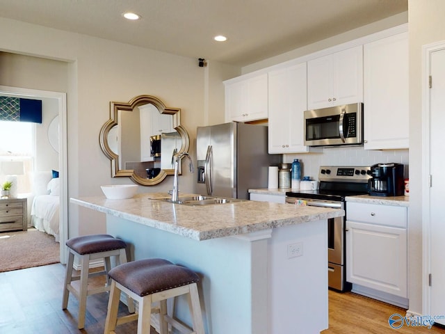 kitchen with sink, a breakfast bar, appliances with stainless steel finishes, a kitchen island with sink, and white cabinets