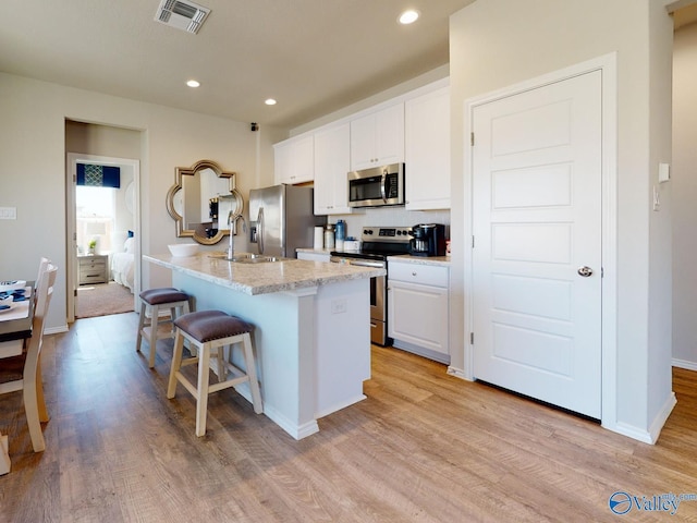 kitchen featuring stainless steel appliances, a breakfast bar, white cabinets, and a center island with sink