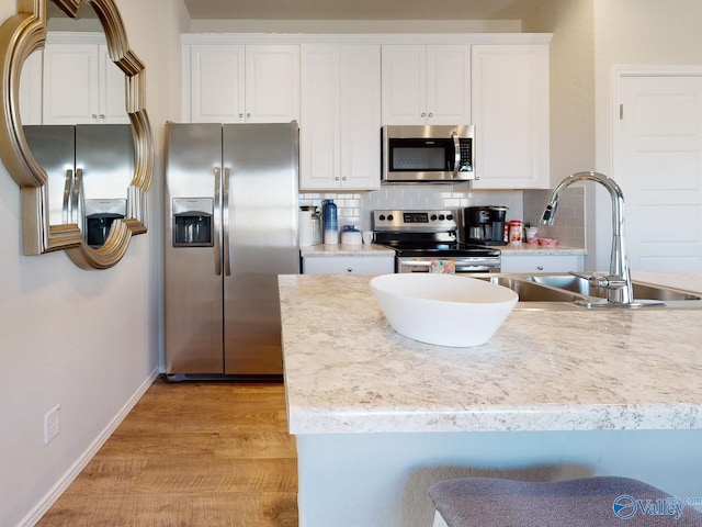 kitchen with white cabinetry, appliances with stainless steel finishes, light hardwood / wood-style floors, and decorative backsplash