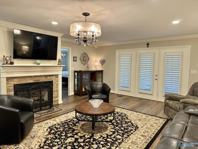 living room with a fireplace, hardwood / wood-style flooring, crown molding, and an inviting chandelier