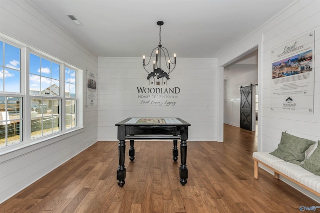 dining area with hardwood / wood-style floors, a barn door, wooden walls, and a notable chandelier