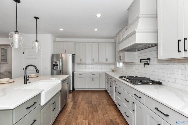 kitchen with pendant lighting, premium range hood, sink, appliances with stainless steel finishes, and tasteful backsplash