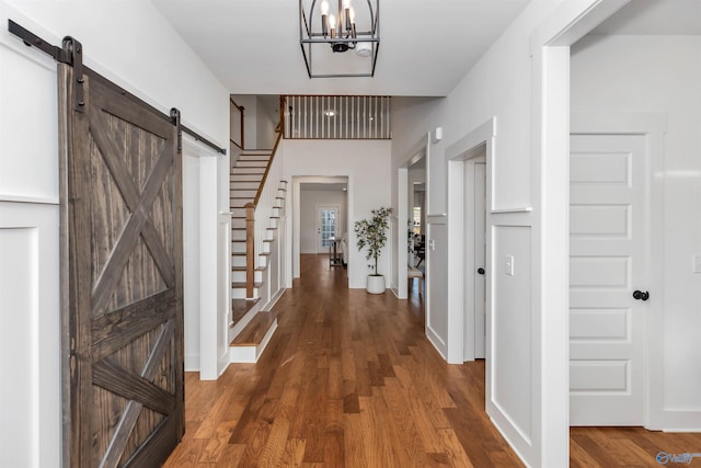 corridor featuring a barn door, dark hardwood / wood-style floors, and an inviting chandelier