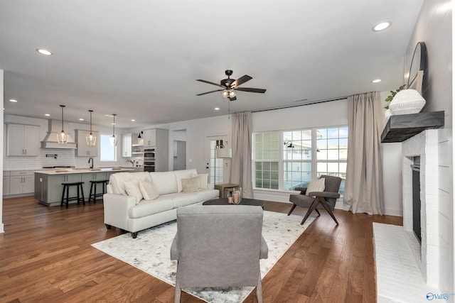 living room with ceiling fan, dark hardwood / wood-style floors, sink, and a brick fireplace