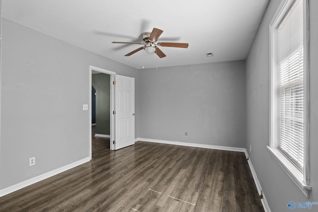 unfurnished room with dark wood-style floors, visible vents, baseboards, and a ceiling fan