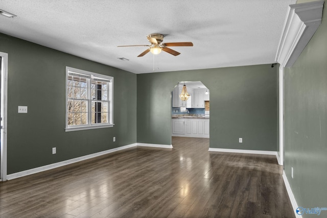 unfurnished living room featuring dark wood-style floors, arched walkways, baseboards, and a ceiling fan