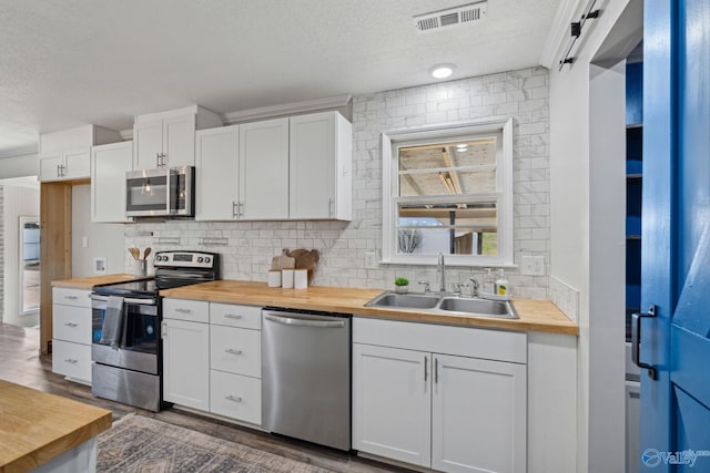 kitchen featuring butcher block counters, white cabinetry, sink, a textured ceiling, and appliances with stainless steel finishes