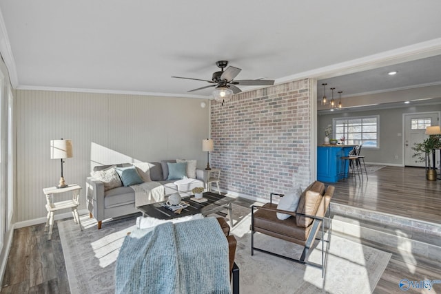 living room with crown molding, ceiling fan, wood-type flooring, and brick wall