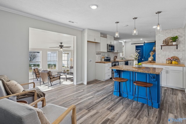 kitchen with hanging light fixtures, stainless steel appliances, a barn door, a breakfast bar, and white cabinets