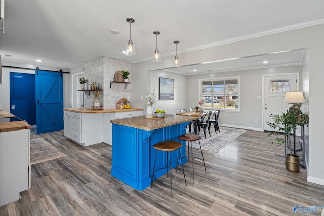 kitchen featuring hanging light fixtures, white cabinetry, a barn door, a kitchen island, and butcher block counters