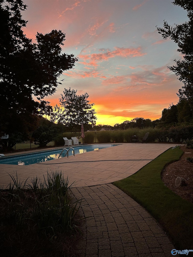 pool at dusk featuring an outdoor pool, a patio, and fence