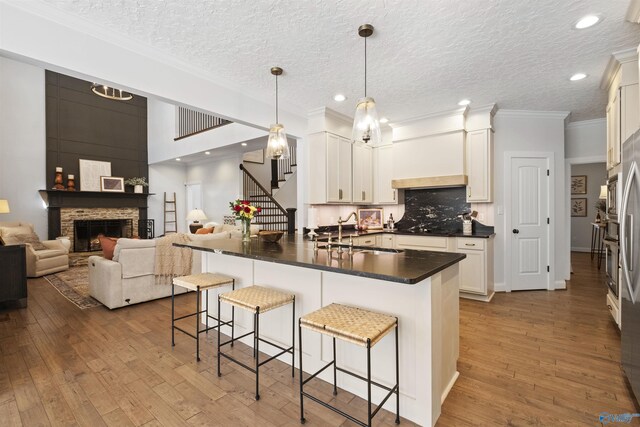 kitchen with dark countertops, a breakfast bar area, a stone fireplace, hardwood / wood-style flooring, and a sink