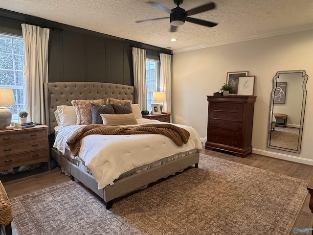 bedroom with a ceiling fan, a textured ceiling, wood finished floors, crown molding, and baseboards