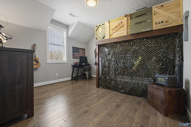 bedroom featuring wood finished floors, baseboards, visible vents, lofted ceiling, and a textured ceiling