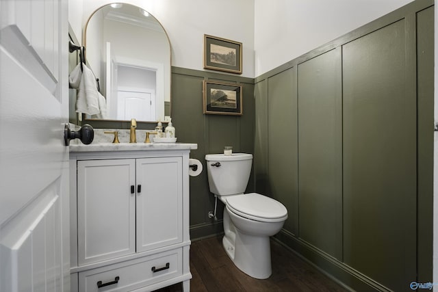 bathroom with toilet, ornamental molding, wood finished floors, a decorative wall, and vanity