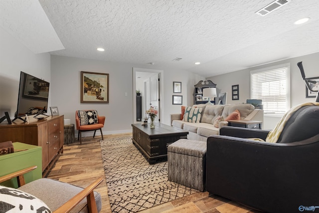 living room featuring visible vents, a textured ceiling, recessed lighting, light wood finished floors, and baseboards