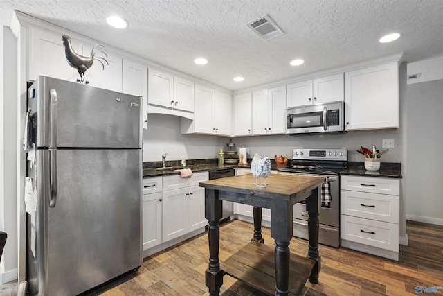 kitchen featuring visible vents, white cabinetry, stainless steel appliances, and wood finished floors