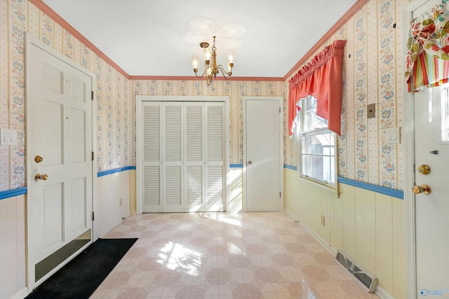 entryway featuring wallpapered walls, visible vents, wainscoting, ornamental molding, and a notable chandelier