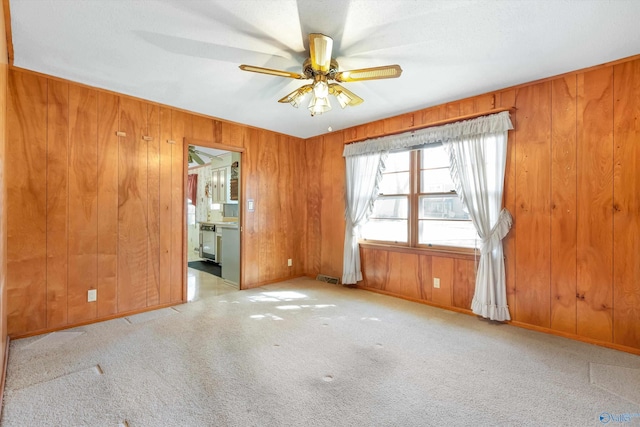 spare room featuring wooden walls, baseboards, visible vents, a ceiling fan, and carpet floors