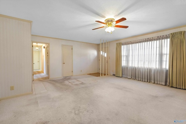 carpeted empty room featuring baseboards, ornamental molding, and a ceiling fan