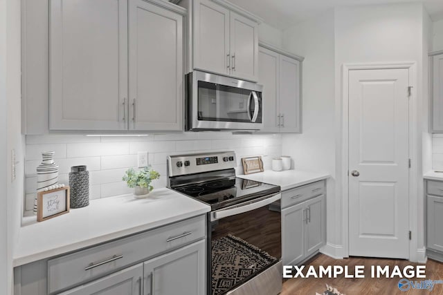 kitchen featuring gray cabinets, appliances with stainless steel finishes, dark hardwood / wood-style floors, and backsplash