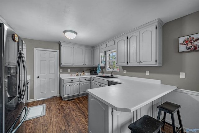 kitchen with sink, stainless steel fridge, dark hardwood / wood-style flooring, kitchen peninsula, and a breakfast bar area