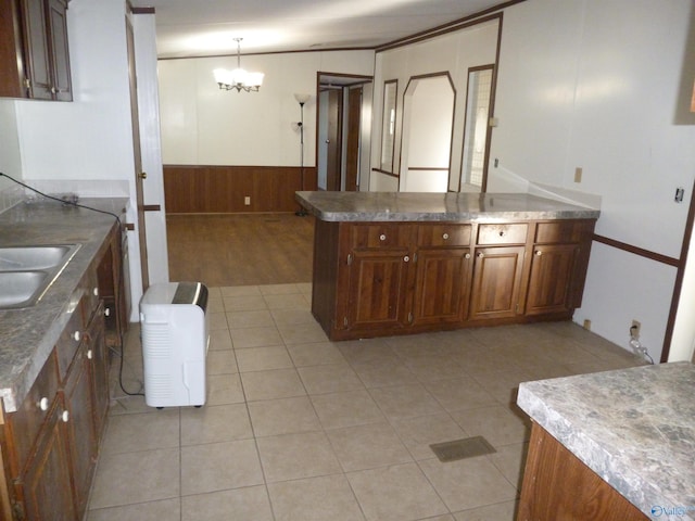 kitchen featuring wood walls, sink, an inviting chandelier, light tile patterned flooring, and hanging light fixtures