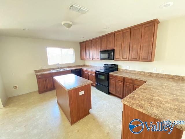 kitchen featuring black appliances, light countertops, a sink, and a center island