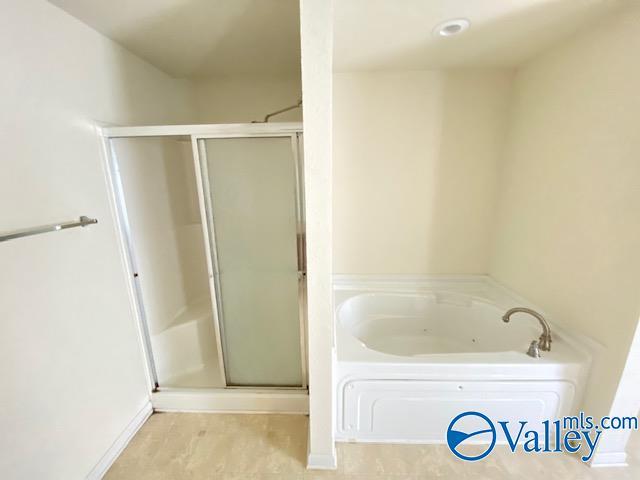 full bathroom featuring a stall shower, a garden tub, and wood finished floors