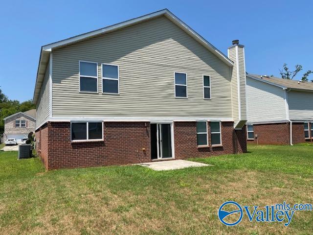 rear view of house with brick siding, central AC unit, and a yard