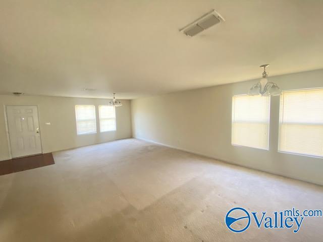 carpeted spare room with visible vents and a notable chandelier