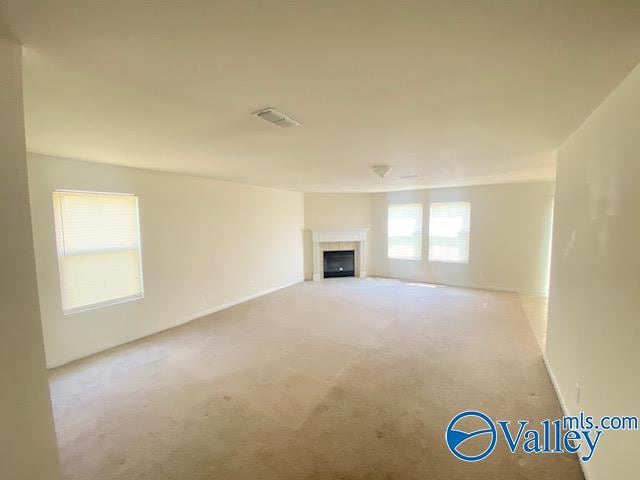 unfurnished living room featuring light colored carpet, visible vents, and a tiled fireplace