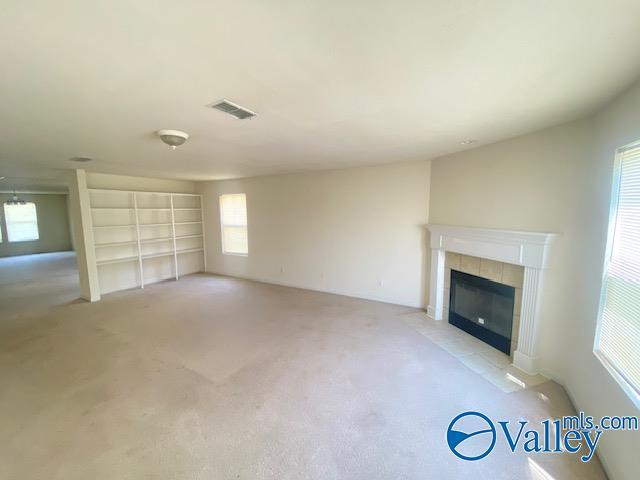 unfurnished living room with light carpet, visible vents, and a tiled fireplace