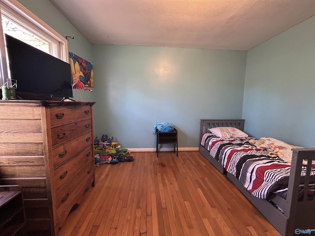 bedroom with a textured ceiling, baseboards, and wood finished floors