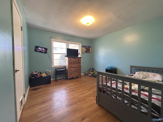 bedroom featuring light wood finished floors, baseboards, and a textured ceiling