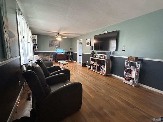 living area featuring ceiling fan, a textured ceiling, baseboards, and wood finished floors