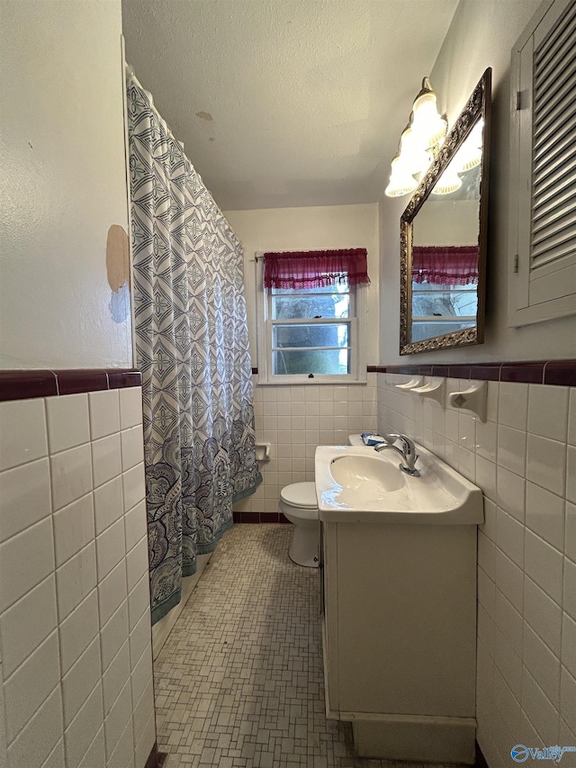 bathroom featuring a textured ceiling, tile patterned flooring, vanity, and tile walls