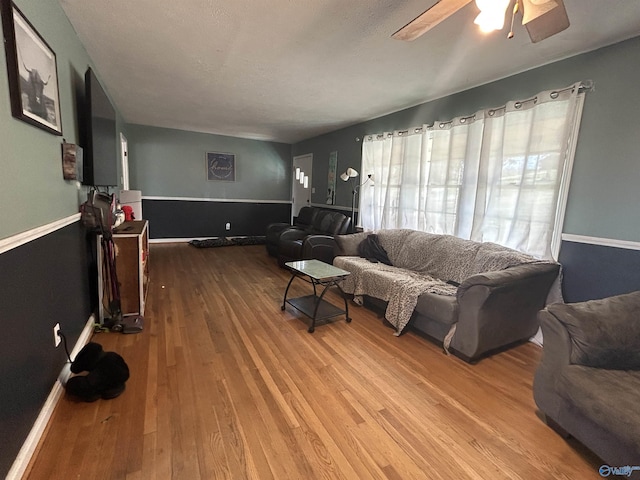 living room featuring a wainscoted wall, ceiling fan, and wood finished floors