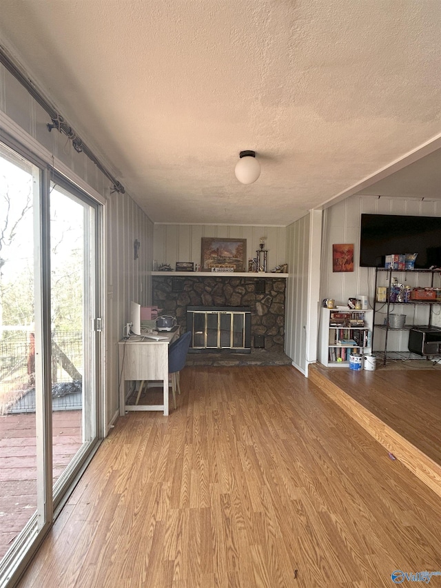 interior space featuring light wood-style flooring, a textured ceiling, and a stone fireplace