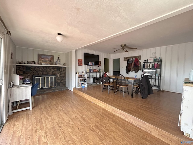 dining space featuring a textured ceiling, ceiling fan, a stone fireplace, and wood finished floors