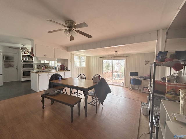 dining room with wooden walls, a ceiling fan, and dark wood-type flooring