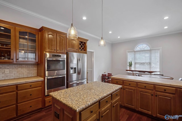 kitchen featuring stainless steel appliances, hanging light fixtures, a center island, brown cabinetry, and glass insert cabinets