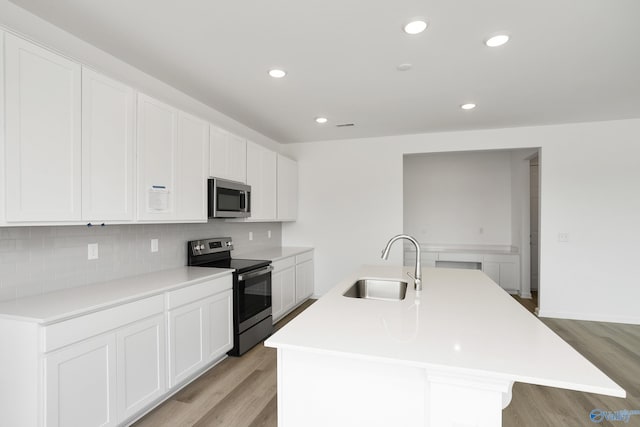 kitchen featuring sink, stainless steel appliances, tasteful backsplash, light hardwood / wood-style floors, and an island with sink