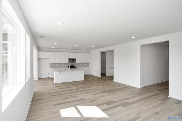 kitchen with stainless steel appliances, light hardwood / wood-style flooring, a center island with sink, and white cabinets